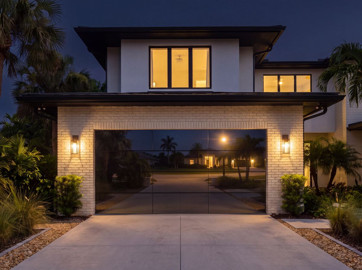 Modern Garage Door at night, mirrored glass panels and the home's illuminated windows glowing warmly against the dusk sky